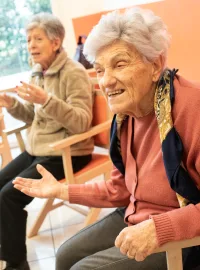 Due signore anziane sorridono e parlano, sedute in un salone