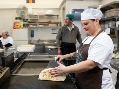 Una cuoca stende una piadina sulla piastra, in una cucina professionale