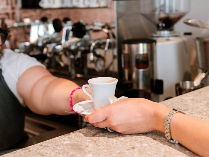 Una mano porge una tazzina di caffè dal bancone del bar.