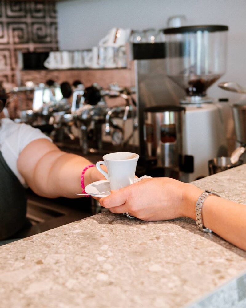 Una mano porge una tazzina di caffè dal bancone del bar.
